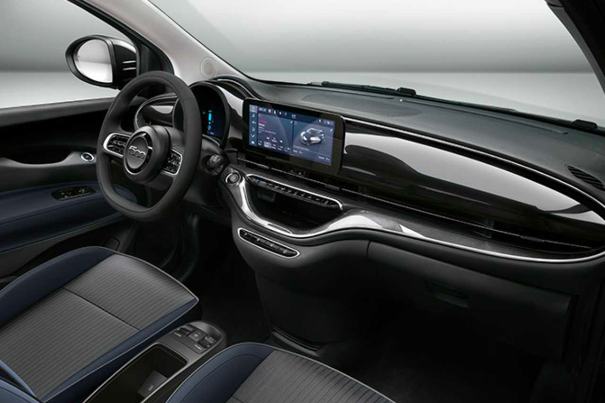 Interni Fiat 500 elettrica, con plancia moderna, volante multifunzione e display touchscreen centrale.