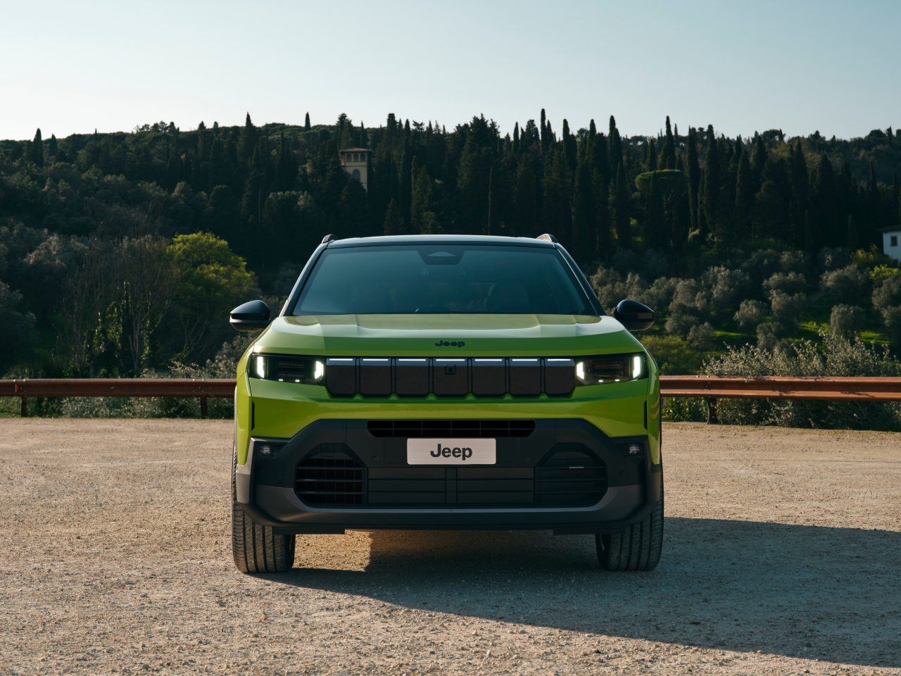 Vista frontale della Nuova Jeep Compass 2025 in colore verde con fari Matrix LED e design rinnovato del frontale, fotografata all’aperto con paesaggio naturale sullo sfondo.