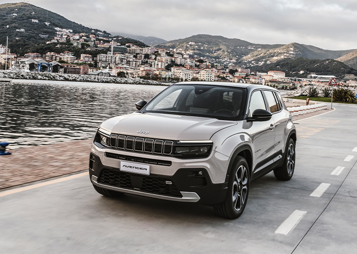 Nuova Jeep Avenger SUV compatto su strada costiera con vista mare, design frontale con griglia Jeep a sette feritoie e fari LED, B-SUV moderno ideale per città e viaggi.
